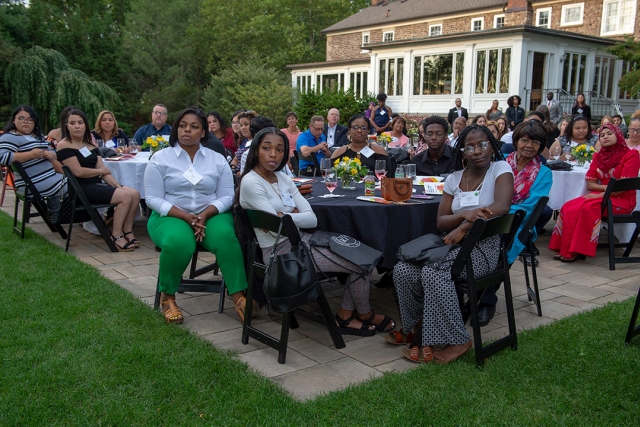 Students at round tables on patio listen to speaker.