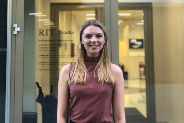 Emily Arnold in front of glass doors with the text "RIT Croatia."
