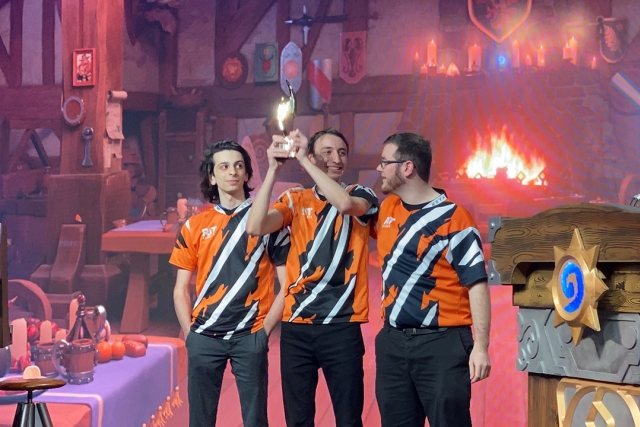 three e-sports players holding up trophy on stage.