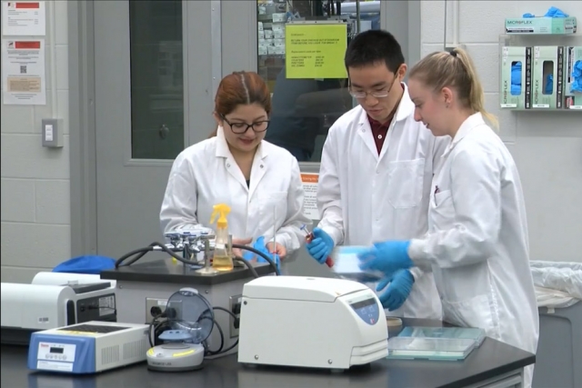 three students wearing lab coats working with pipette.