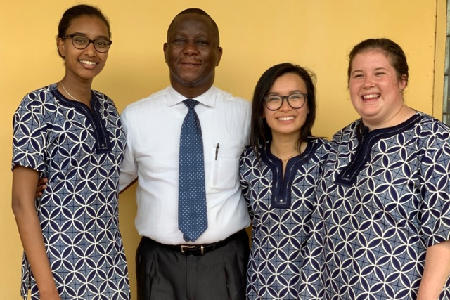 professor standing with three students wearing traditional garb.