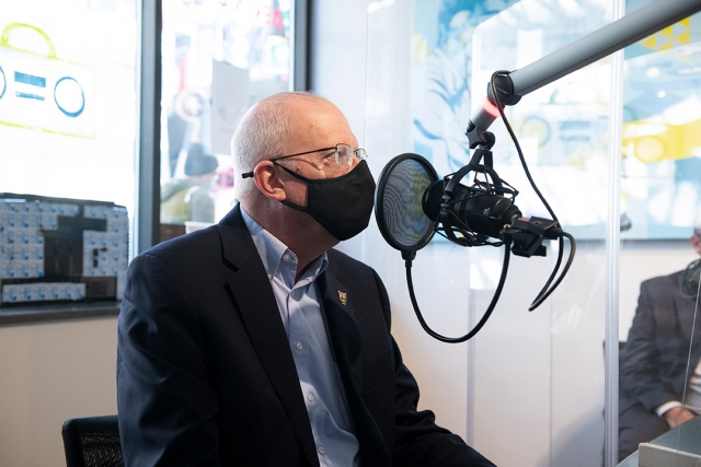 RIT president wearing a facemask and talking into a microphone in a radio station.