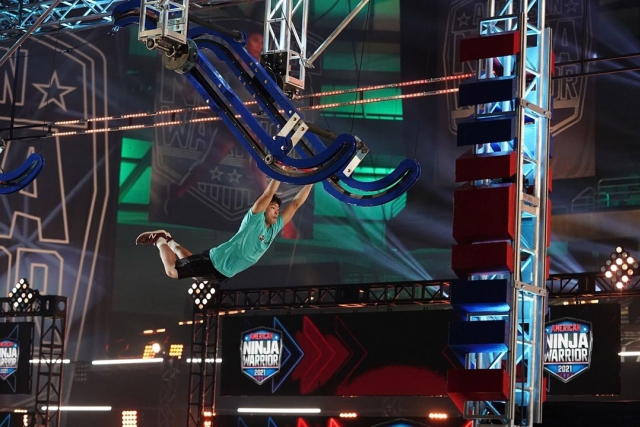 student swinging from a large arm contraption in a ninja warrior contest.