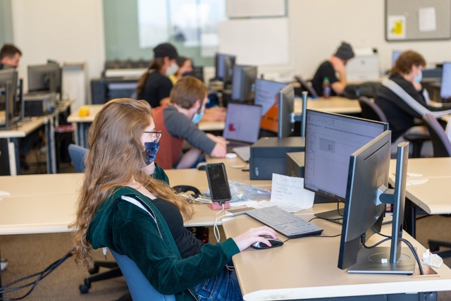 students wearing masks sitting at desks in a classroom.