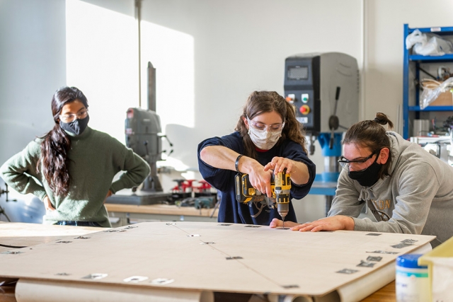 student using a power drill to drill holes into a piece of particle board.