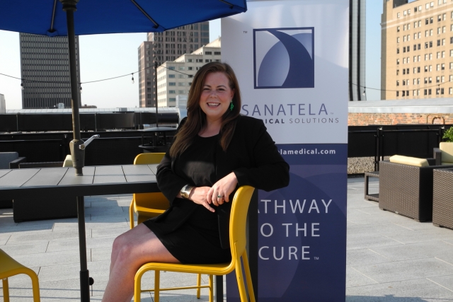 Erin Crowley Ellis sitting at a desk and smiling in front of a sign that says "Sanatela Medical Solutions."