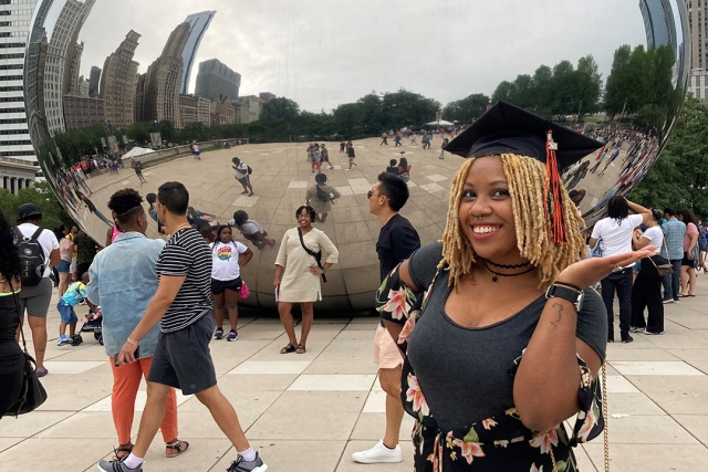recent graduate standing in front of the giant, reflective jelyl bean statue in Chicago.