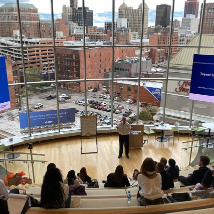 meeting in a large room with a rounded wall of windows facing a city landscape.