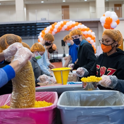 students working in an assembly line to fill bags with ingredients for meals.