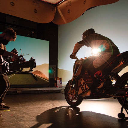 student in a studio filming a person sitting on a motorcycle.