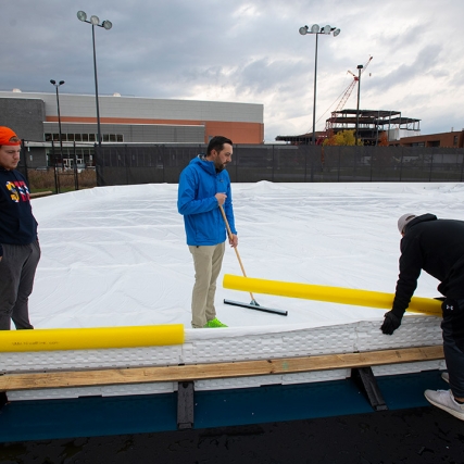 three people working on setting up an outdoor ice rink.