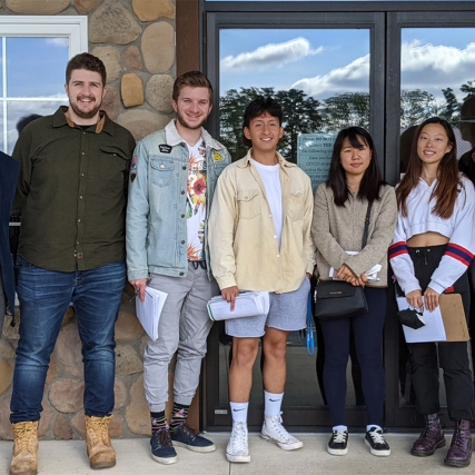 professor standing outside a cobblestone building with six students.