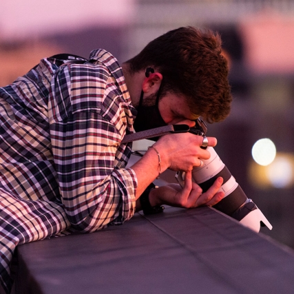 student leaning over a ledge taking a photo with a telescopic lens.