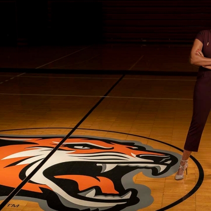 athletic director standing near Tiger logo on basketball court.
