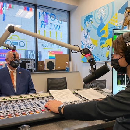 RIT President Munson wearing a mask and speaking into a microphone in a radio station.