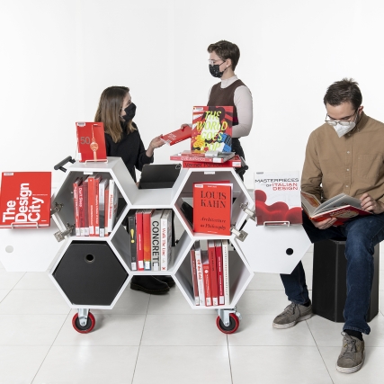 A collection of design books displayed on the Hexacart with students gathering around it.