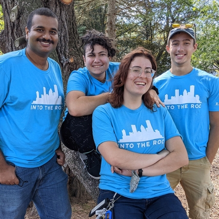 four student volunteers posing for a photo on a tree branch.