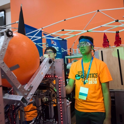 students on robotics team about to use a robot to launch an orange ball.