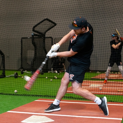 athlete in a batting cage swinging a baseball bat.