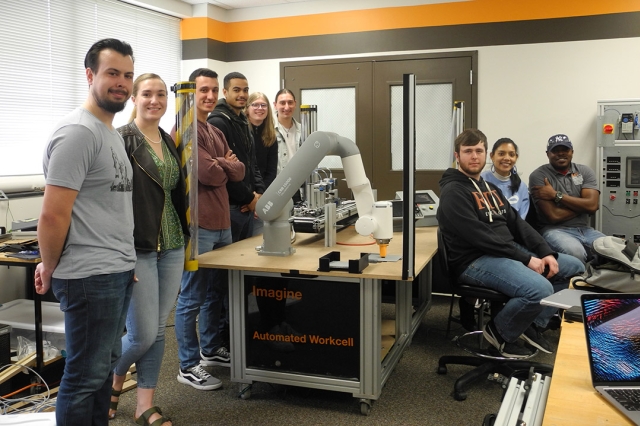 nine students sitting in a lab with a new robotic arm assembly.
