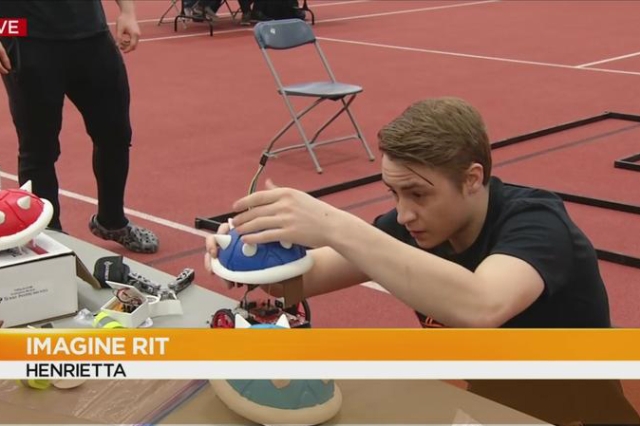 A male student makes adjustments to a robot with a blue spiky shell on top and text is overlaid that says, "IMAGINE RIT HENRIETTA"