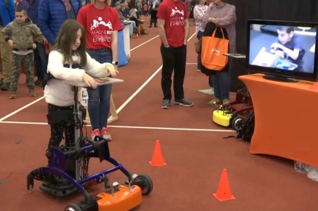 A girl in a standing wheelchair interacts with a screen on display in the Gordon Field House at Imagine RIT.