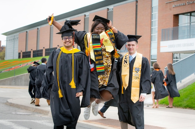 three graduating students wearing their cap and gown and important sashes.
