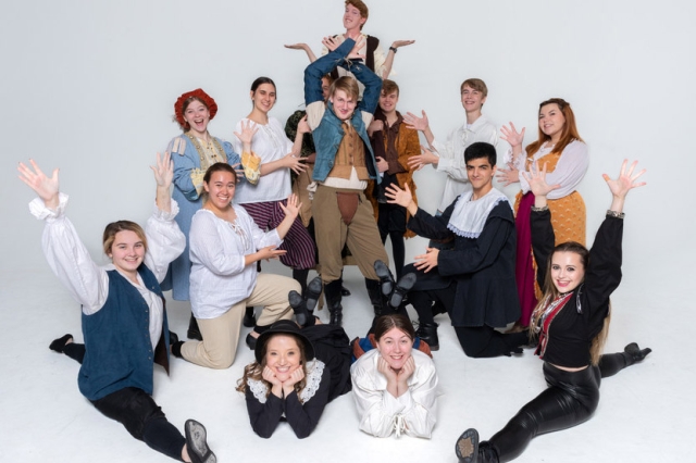 cast of a play posing with their hands in the air.