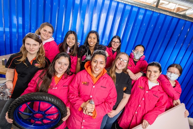 group of eleven college students holding components to an electric car.