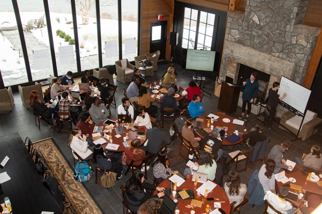Over head picture of graduate school workshop. Students at tables with work supplies.