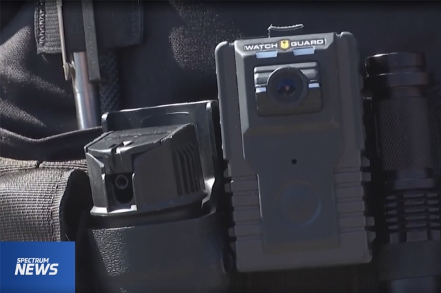 screenshot from a Spectrum News clip showing a closeup of a body camera on a police officer.