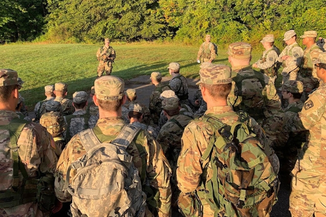 R O T C army cadets in a field listening to their instructor.