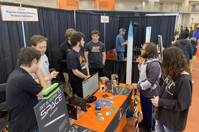 college students around a display table about rockets.