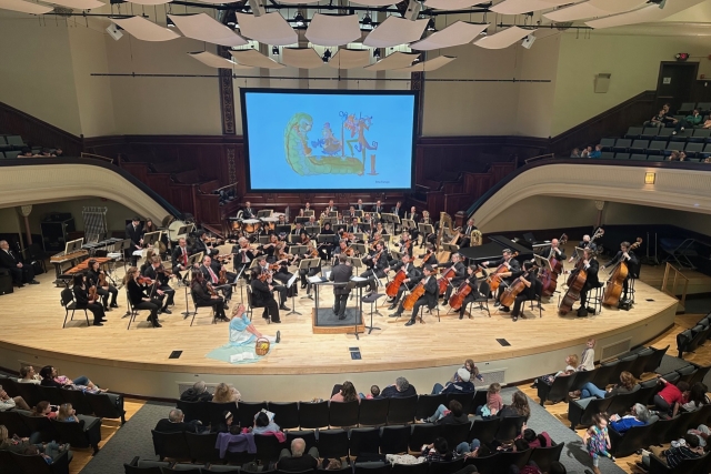An orchestra plays a concert with a projected illustration by an RIT student on a screen.