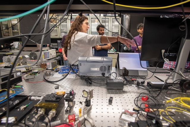 researcher standing next to a desk with various pieces of lab equipment.