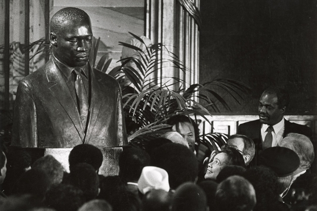 a black and white image of a group of people facing Coretta Scott King as she reacts to an MLK portrait being unveiled