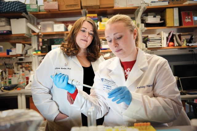 a student and professor are seen in lab coats using a pipette.