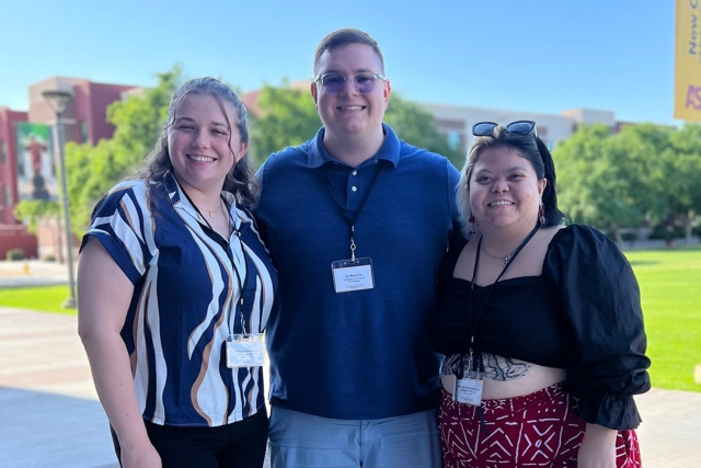 Three students stand in an open area of a university.