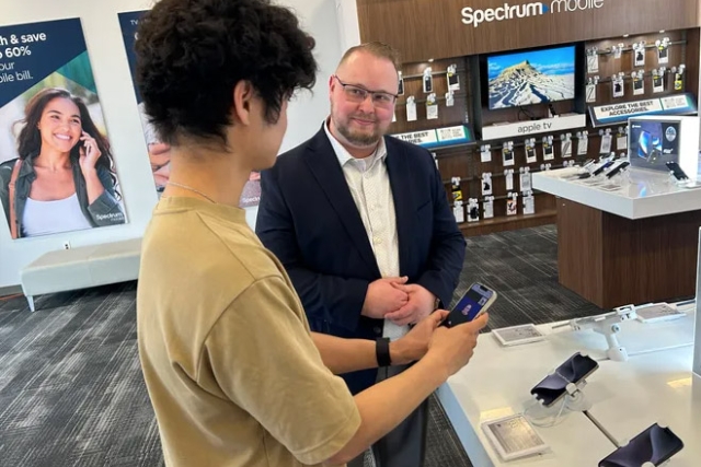 Trent Hobble is shown holding a phone trying out an ASL Video Relay Service in a local Spectrum store.
