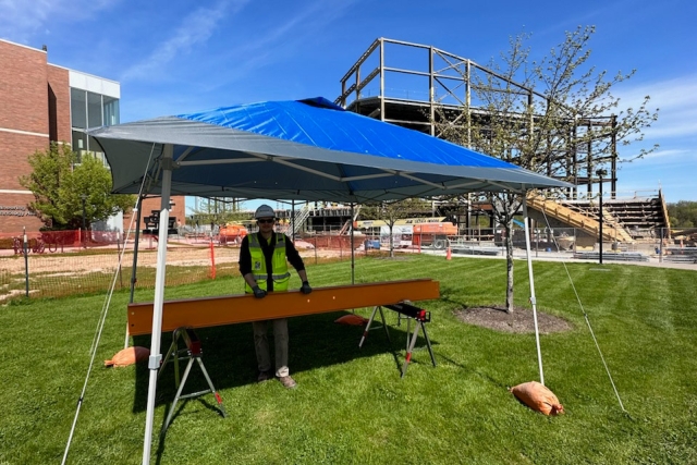 a man in a hard hat stands under a popup tent behind a 12 foot steel beam.