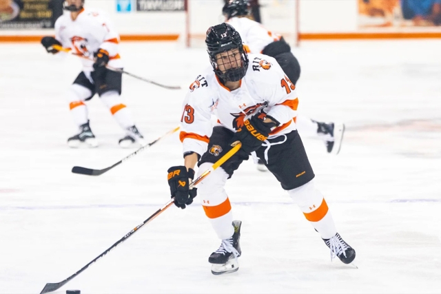 An action shot of Addie Alvarez skating on the ice with a hockey stick in hand, wearing her RIT team uniform.