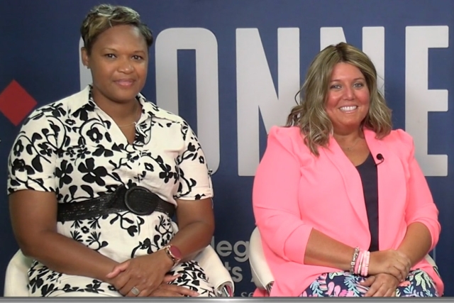 Two women sit in front of a blue and white background for an interview.