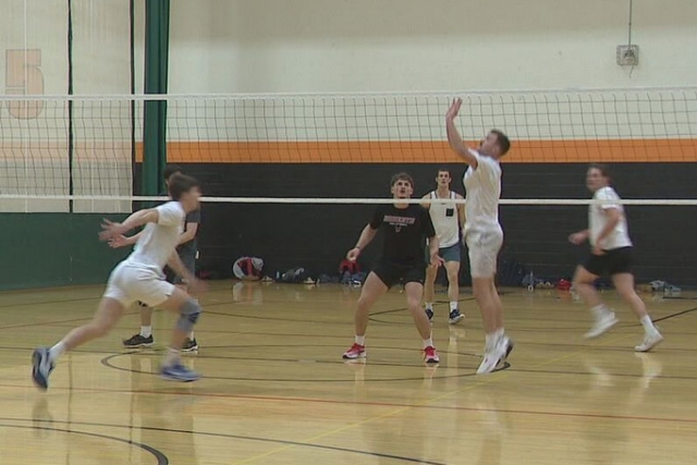 a group of men are shown playing a game of volleyball in a gymnasium.