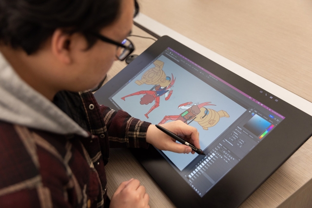 Person uses a stylus on a digital drawing tablet to illustrate cartoon robots.