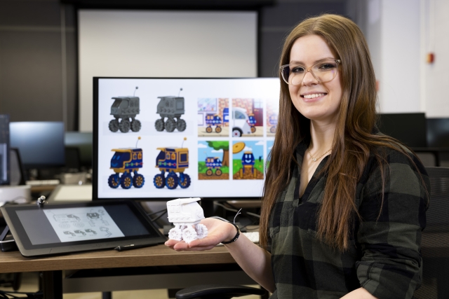 Ava Guarino holds up her 3D-printed toy truck, with a computer screen showing the designs in the background.