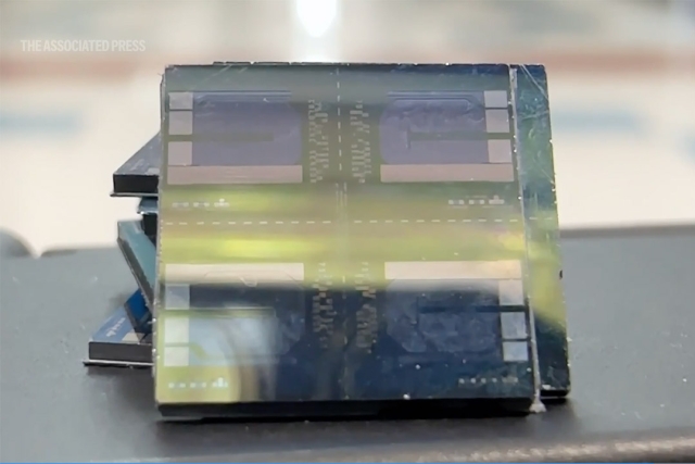 Close-up of a small, layered rectangular microchip with grid patterns reflecting blue and green colors.