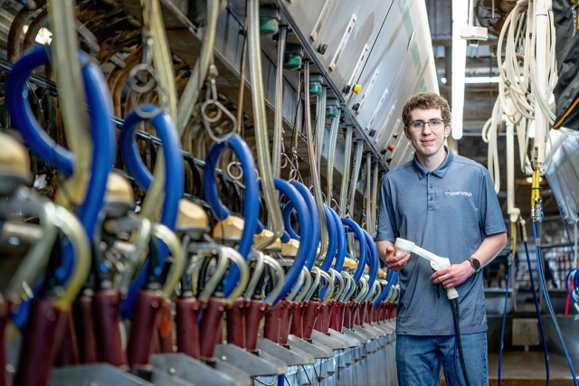 Person in a dairy milking parlor holding a milking hose.