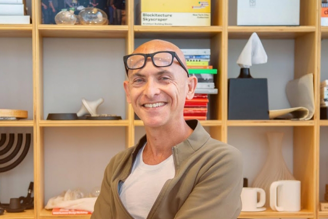 Smiling man standing in front of a bookshelf, wearing glasses on his head.