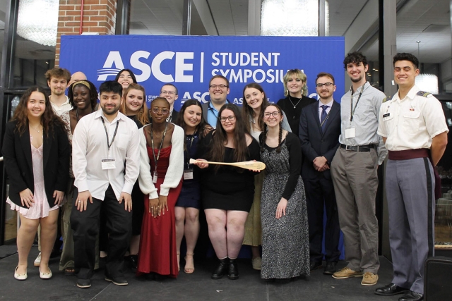a team of young adults stand in front of an ASCE sign in a building.