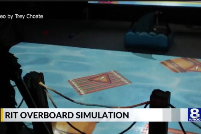 a video game is shown displayed on a floor with a chyron displaying the text R I T overboard simulation at the bottom.